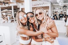 three beautiful young women standing next to each other in front of a bar with people