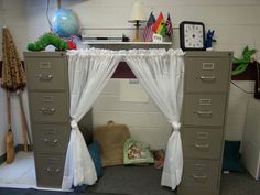 an office cubicle with drawers and curtains on the top, in front of a clock