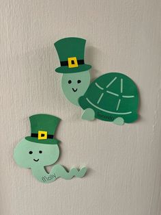 two green paper cutouts with hats on them, one turtle wearing a lepreite hat