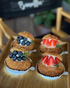 four cupcakes with strawberries and blueberries on them sitting on a wooden tray