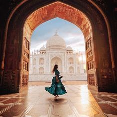 a woman is walking through an archway towards the tajwa mosque in india, where she's wearing a long blue dress