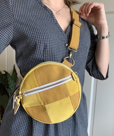 a woman in a blue dress is holding a yellow fanny bag with zippers on it