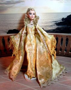 a doll is standing on a balcony overlooking the ocean and water, wearing a golden dress