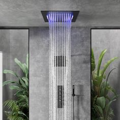 a shower head with water running down it's side and plants in the background