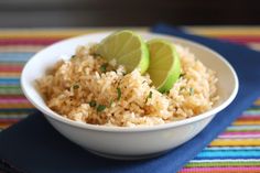 a white bowl filled with rice and limes on top of a colorful table cloth