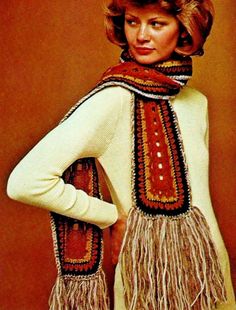 a woman is wearing a scarf with fringes on it and standing in front of a brown wall