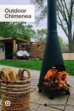 a fire pit sitting on top of a sidewalk next to a basket filled with wood