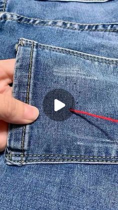 someone is pulling the red string out of their jeans pocket with their thumbnails