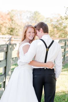 a bride and groom embracing in front of a fence