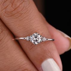 a woman's hand with a diamond ring on her finger and white nail polish