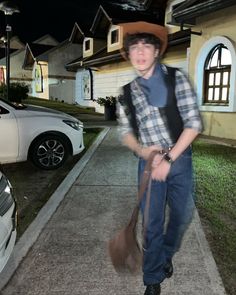 a young man wearing a hat and carrying a bag walks down the street at night