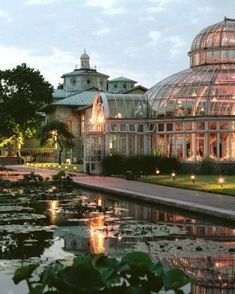 a large glass building sitting next to a pond with lily pads on it's sides