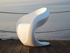 a white chair sitting on top of a wooden floor next to the ocean and a rope