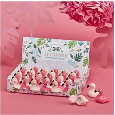 pink flamingos are lined up in front of a card board box and some flowers