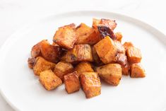 a white plate topped with cubed potatoes on top of a marble countertop next to a knife and fork