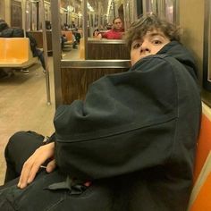 a young boy sitting on a train seat covered in a black jacket and covering his face