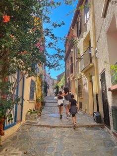 two girls walking down the street in an alleyway with houses and trees on either side