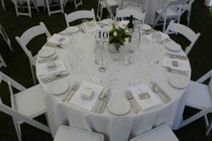 the table is set with white linens and place settings for guests to sit at