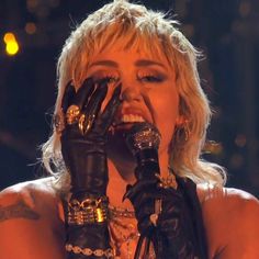 lady in black leather gloves holding her hands up to her face while singing into a microphone