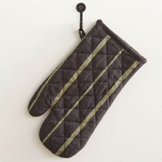 an oven mitt hanging from a hook on a white wall with a black and gold stripe design