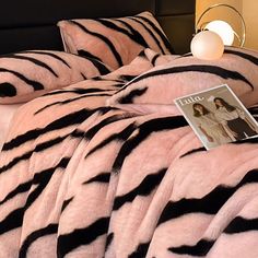 a bed covered in pink and black zebra print sheets with an album on top of it