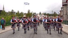 a group of men in kilts marching down a street with people standing around them