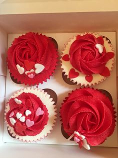 four cupcakes in a box decorated with red and white frosting, hearts and flowers