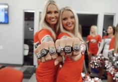 two women in orange shirts pointing their fingers at the camera with cheerleaders behind them