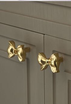 two gold bow knobs on the front of a white cabinet