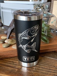 a stainless steel yeti tumbler sitting on top of a wooden table next to rocks