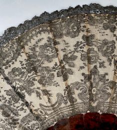 an old lace fan is sitting on the floor next to a tablecloth covered wall