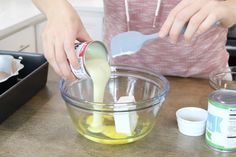 a woman mixing ingredients in a bowl on top of a wooden table with utensils