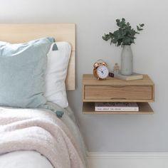 a nightstand with an alarm clock on it next to a bed and a potted plant