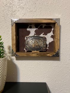 a cow print in a wooden frame hanging on the wall next to a potted plant