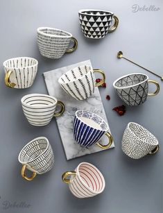 coffee cups and saucers are arranged on a marble slab with gold handles, which also have geometric designs