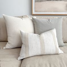 a couch with several pillows on it in front of a framed painting and coffee table