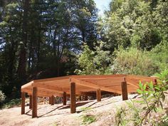 a group of wooden benches sitting on top of a dirt field next to forest filled with trees