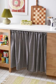 a black and white checkered curtain hanging on a kitchen counter next to a lamp