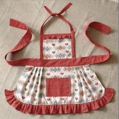 a red and white apron with flowers on it sitting on top of a bed next to a pillow