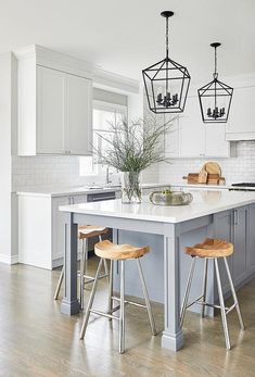 a kitchen island with three stools in front of it and two lights hanging from the ceiling