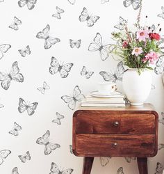 a white vase filled with flowers sitting on top of a wooden table next to a wall