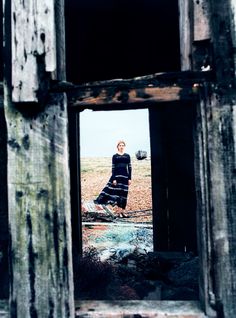 a woman standing in an open door to a wooden structure with peeling paint on it