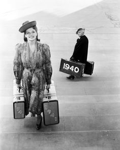 a woman carrying two suitcases while standing next to a man in a suit and hat