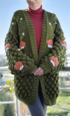 a woman wearing a green knitted cardigan with red and white mushrooms on it