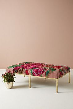 a pink and green floral print footstool next to a potted plant