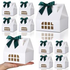 a hand holding a small white box with green ribbon on it and six smaller boxes in the shape of houses