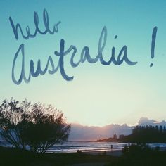 the words hello australia are written in blue ink on a background of trees and mountains