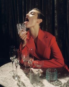 a woman sitting at a table with wine glasses in front of her and mouth open