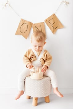 a baby is sitting on a stool with a cake in front of him and the words one above it