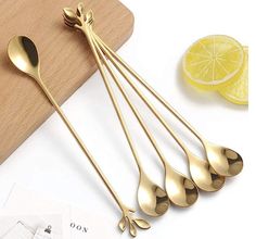 five gold spoons sitting on top of a wooden cutting board next to lemon slices